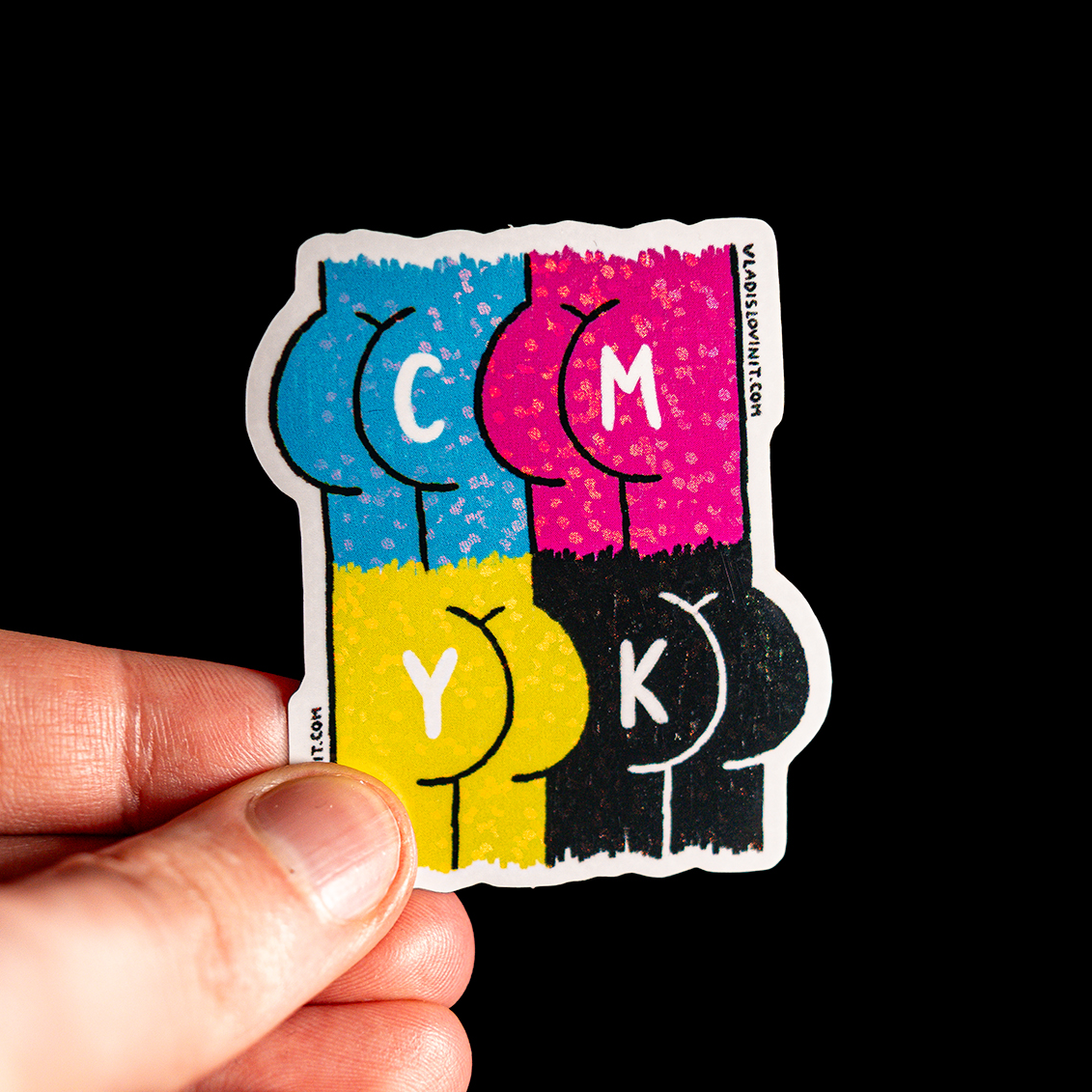 Hand holding a sticker with four stylized, colorful abstract shapes labeled "C," "M," "Y," and "K" on a black background.