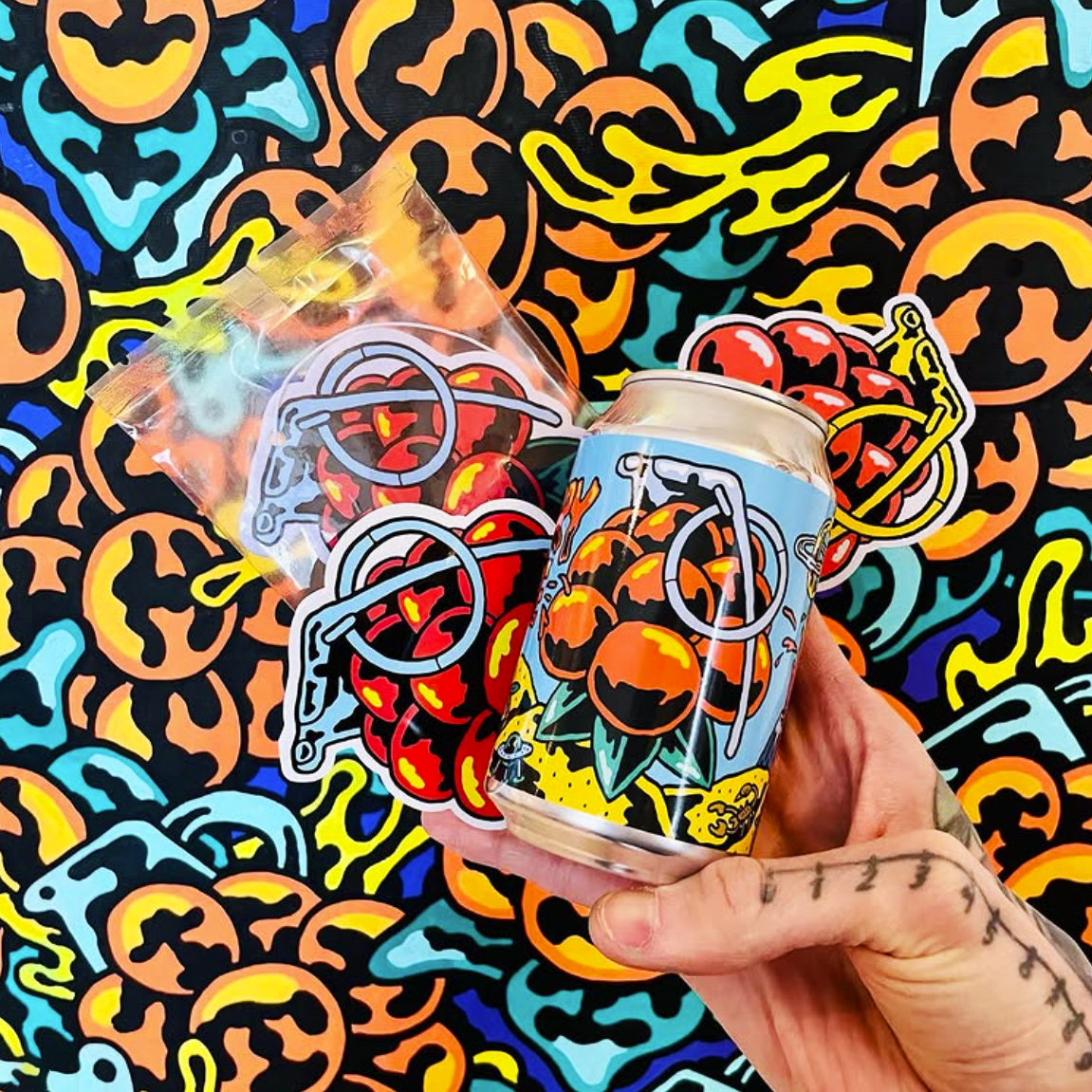 Hand holding a cloudberry grenade soda, surrounded by vinyl stickers, against a colorful, abstract background.