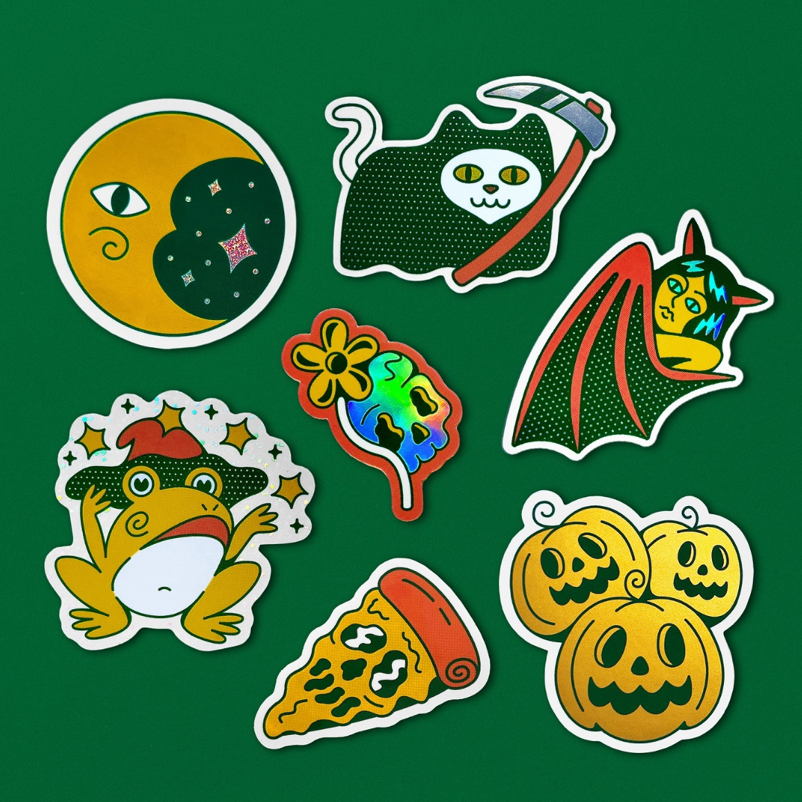 A collection of colorful halloween stickers featuring a moon, cat, bat, frog, skull with a flower, pizza slice, and pumpkins on a green background.