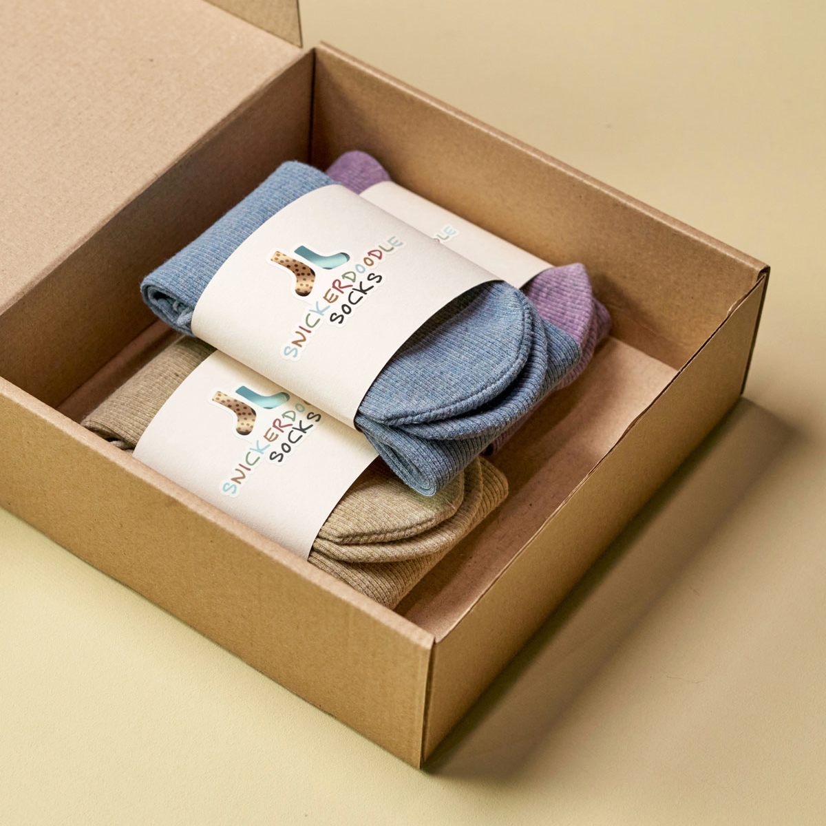 Open cardboard box with three pairs of colorful socks, each wrapped with a lable and die cut sticker.