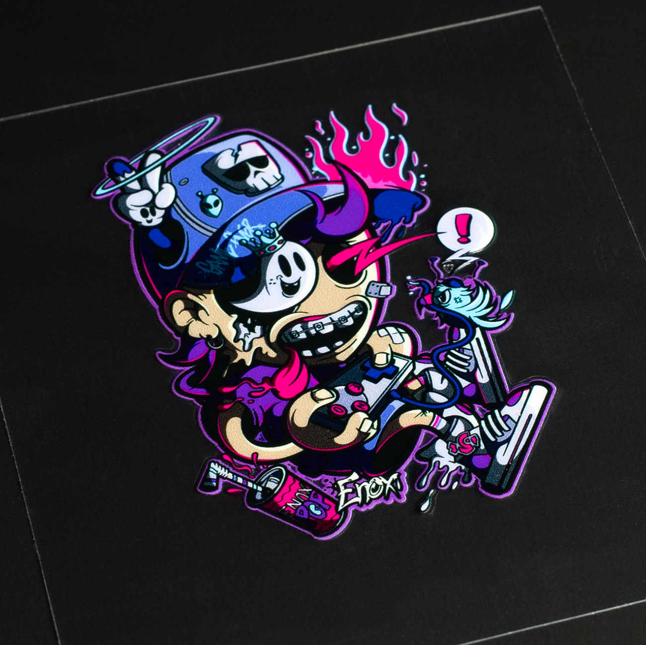 Colorful cartoon transfer sticker with a cap, holding a skateboard and a small creature. The design is vibrant with skulls and flame accents.