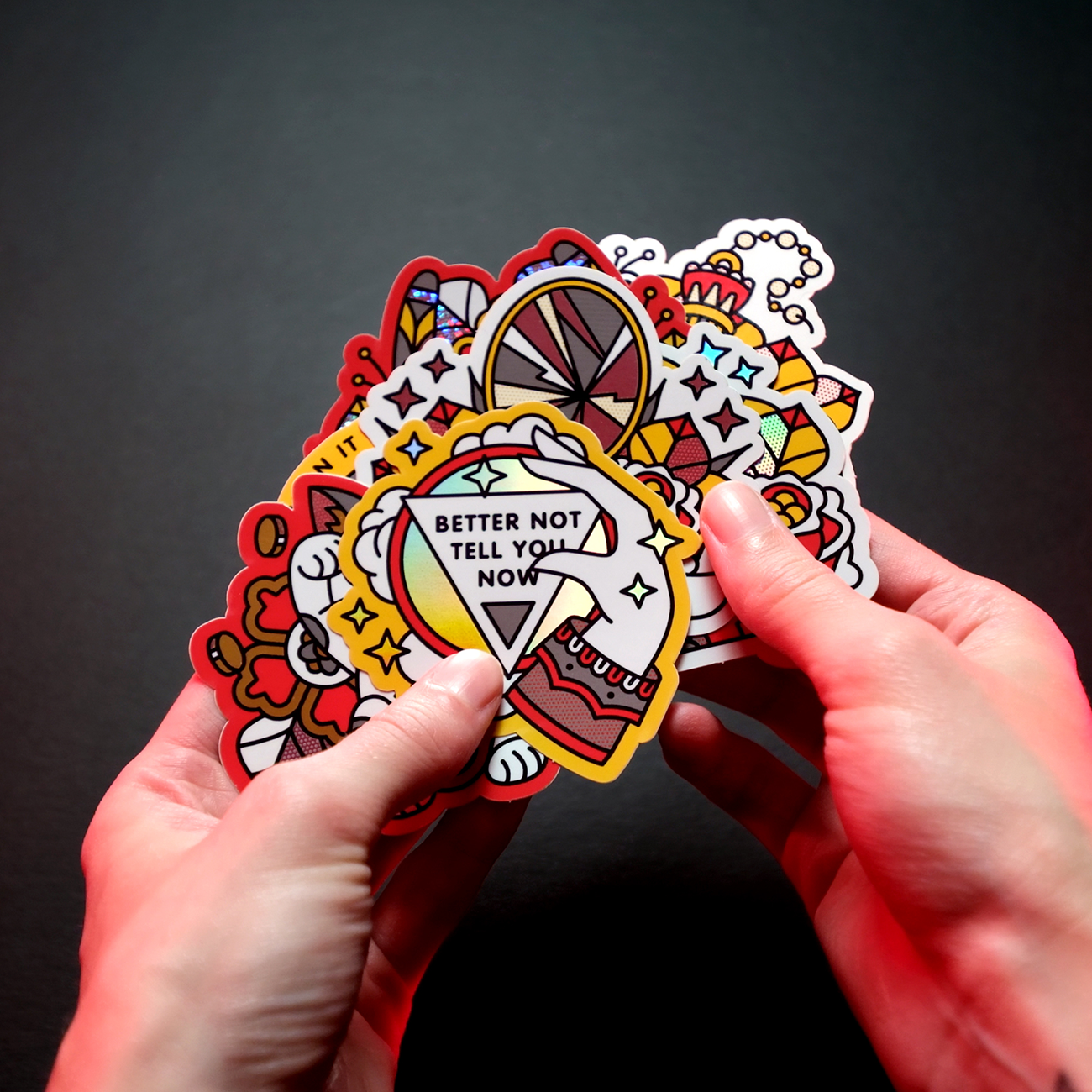 Hands holding colorful, cartoon-style die cut stickers with various designs, from a custom sticker pack.