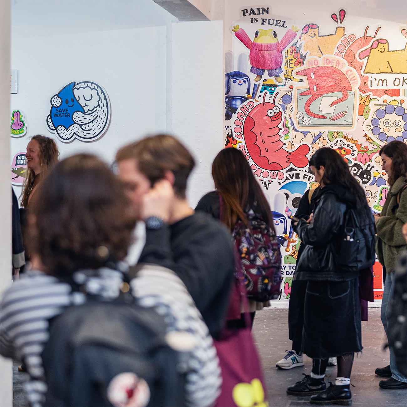Visitors at an art exhibition talking, behind them artwork made of wall stickers hanging on display.