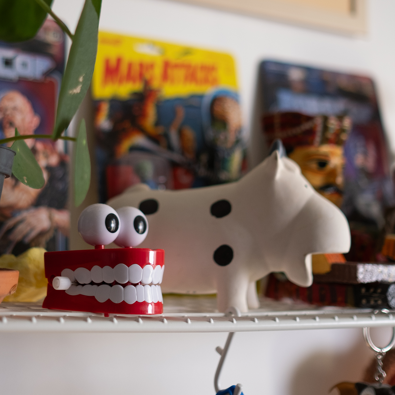 red toy mouth and beige toy cow standing on a white shelf, with comic books and various other toys in teh background