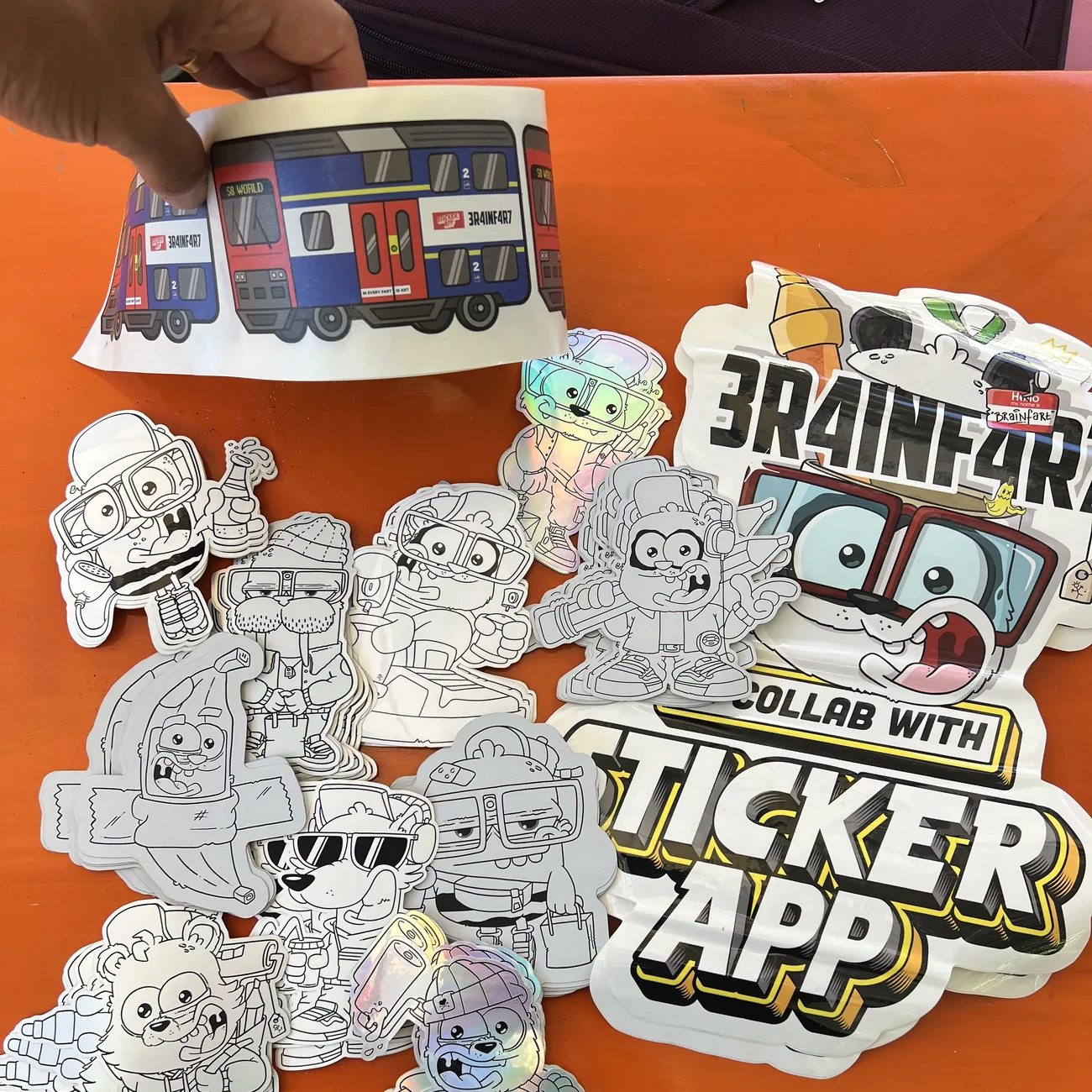 Brainfart x StickerApp S8 World train label with the sign "In every fart is art", held above black-and-white die-cut stickers