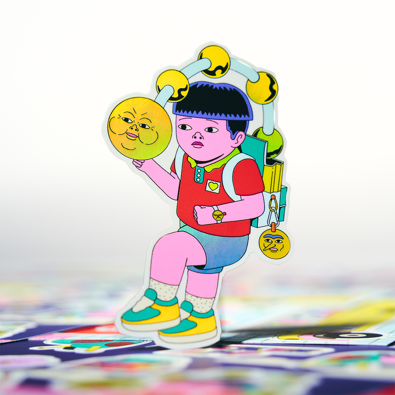 A colorful sticker of a man holding a ball with a face, placed on colorful sheets, against a white bakground