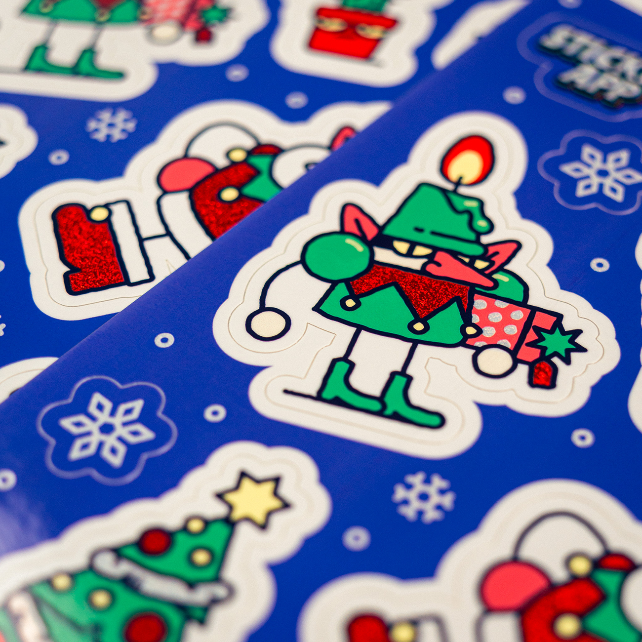 Candle christmas creeper printed on a blue sticker sheet on Pixie Dust, surrounded by other sheets.