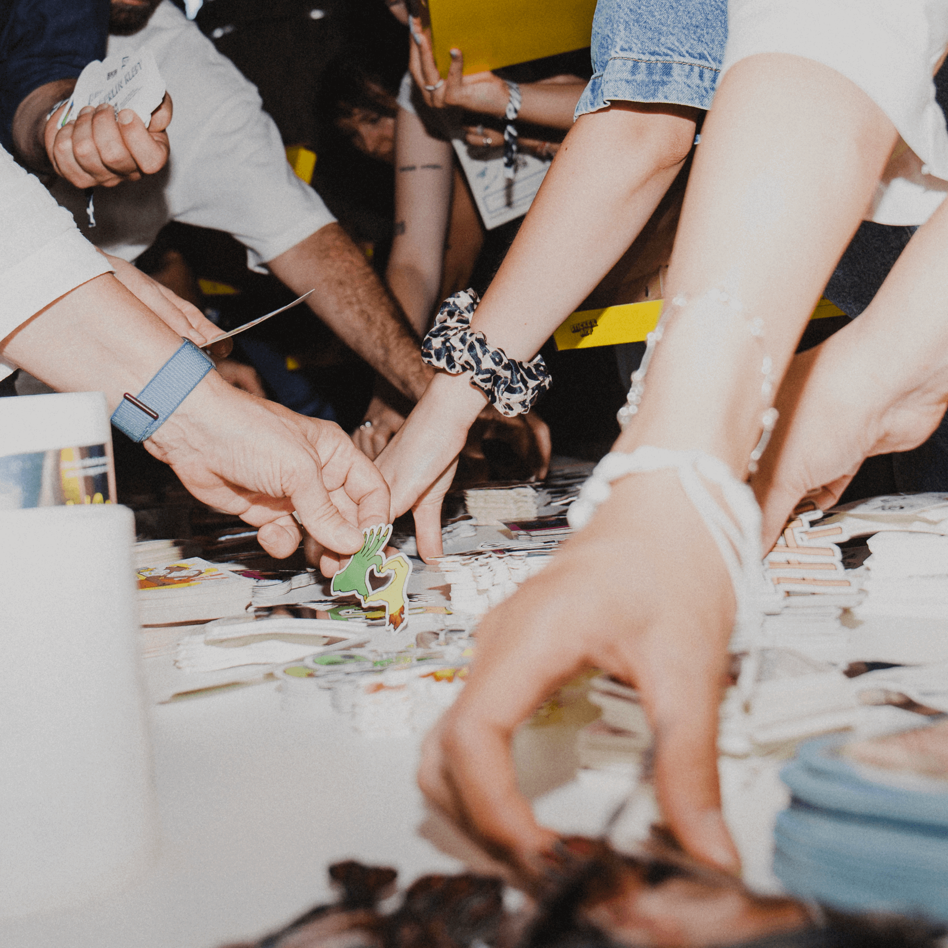 People reaching across a table, picking up various colorful stickers.