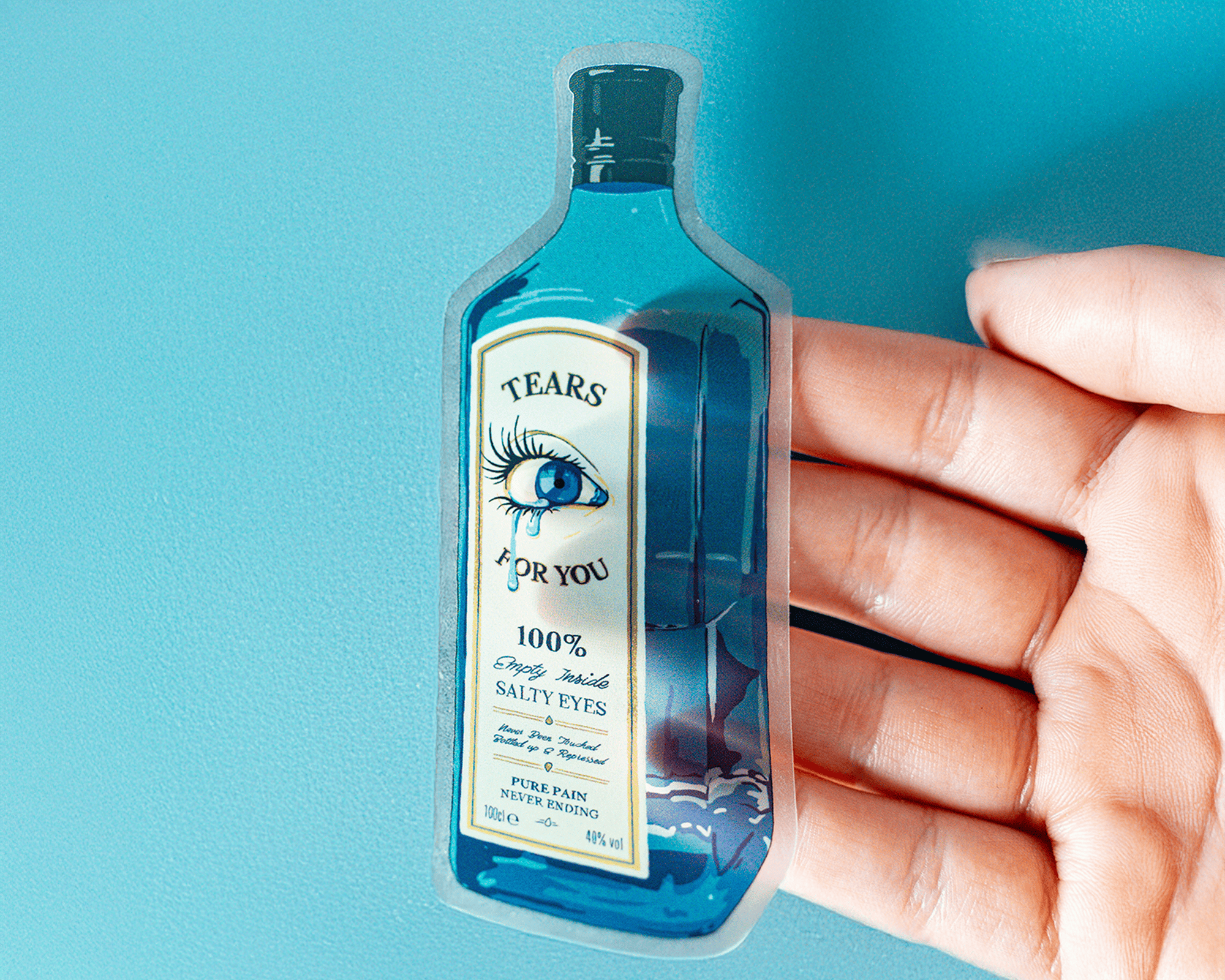 Hand holding a transparent sticker of a blue bottle labeled "Tears for You" with an eye illustration and text about salty tears.