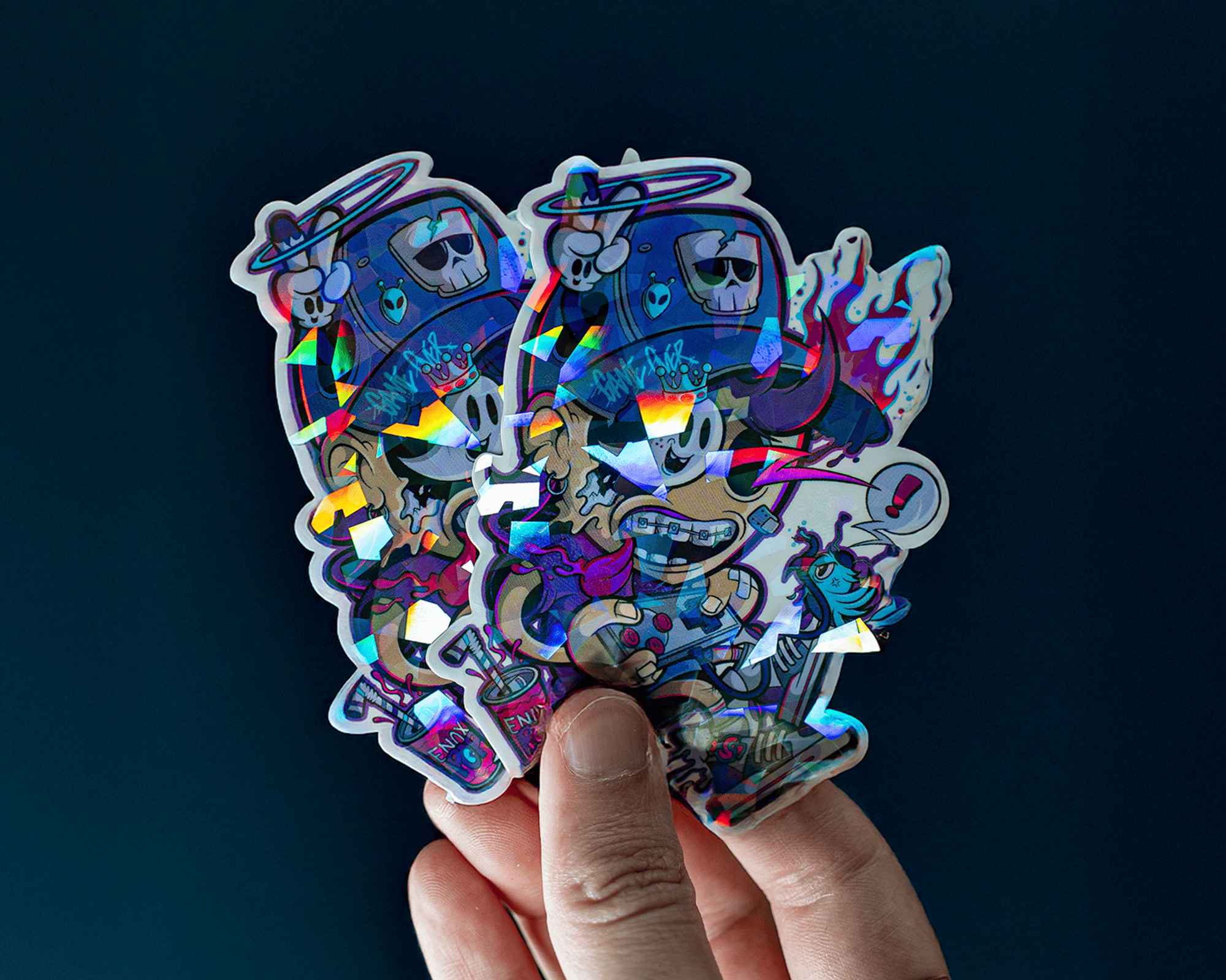 Hand holding colorful, holographic cracked ice stickers featuring cartoon characters with hats, skulls, and vibrant patterns against a dark background.