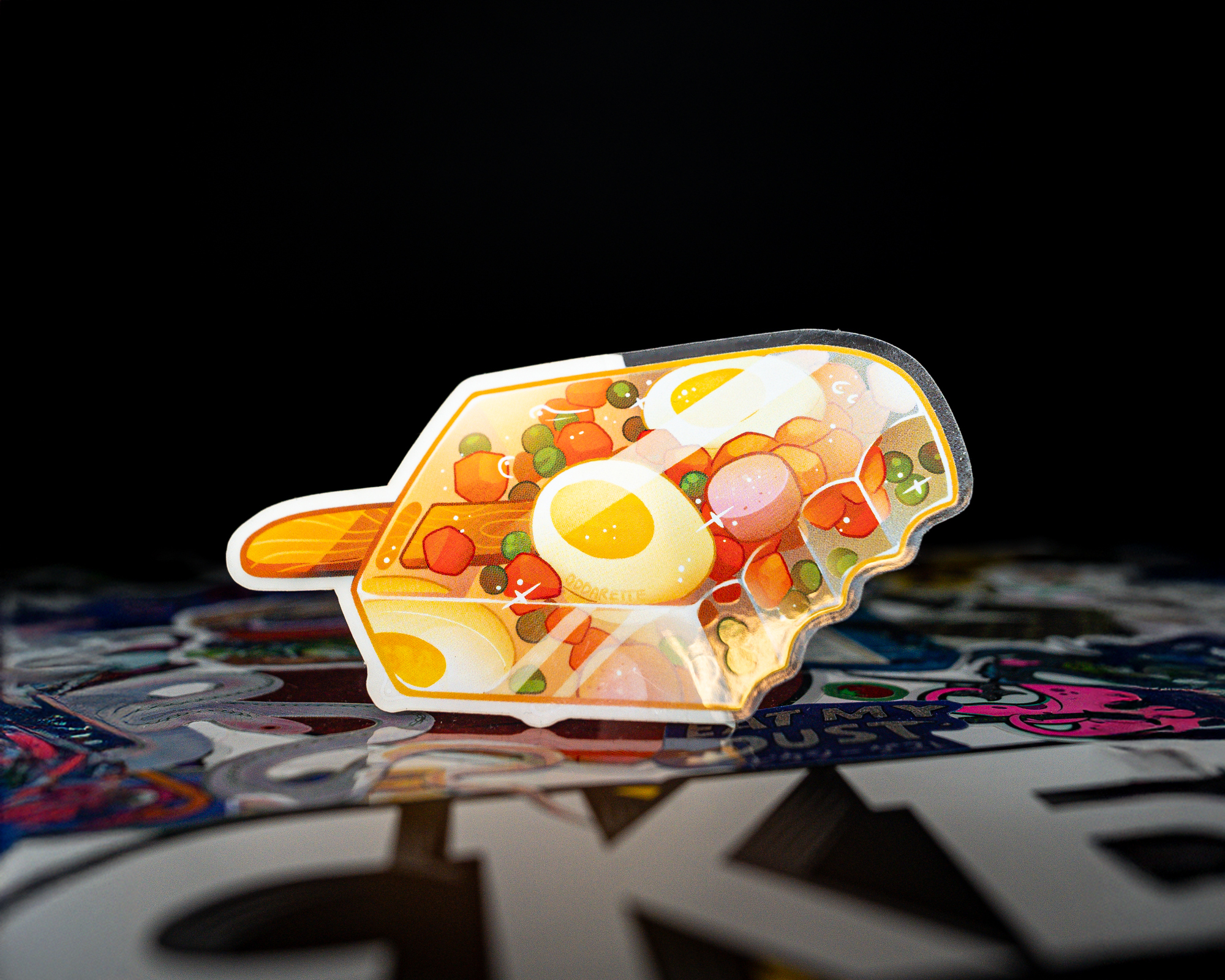 A Transparent sticker shaped like a popsicle, featuring illustrations of eggs, vegetables, and a wooden stick, set against a dark background.