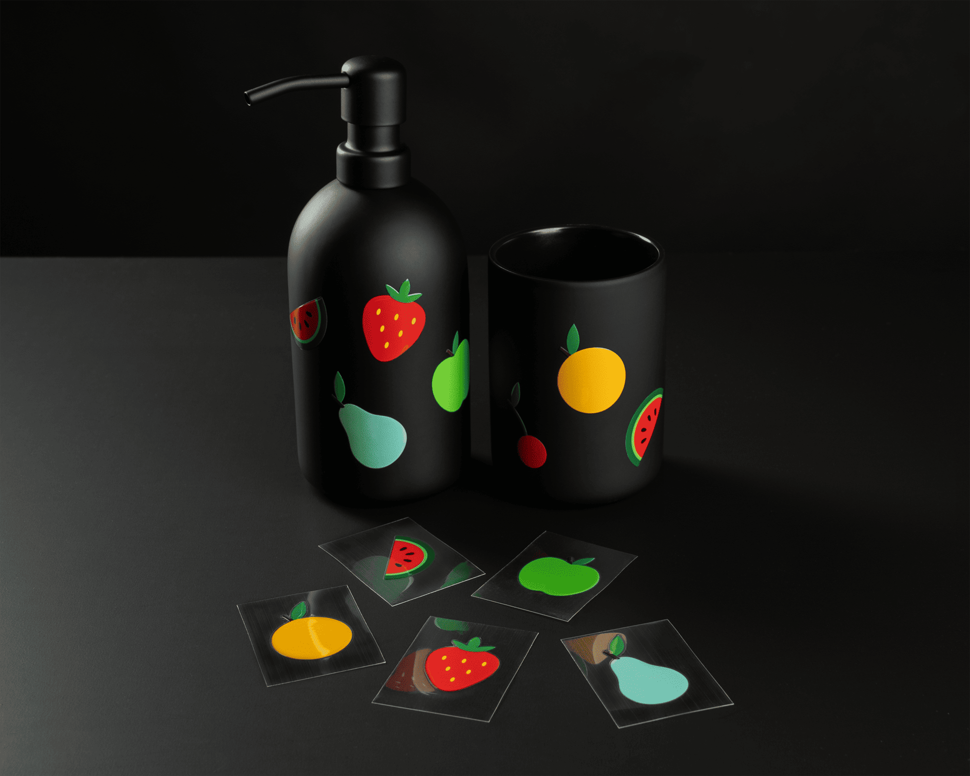 Black soap dispenser and cup with fruit designs, surrounded by fruit-themed uv dtf stickers on a dark surface.