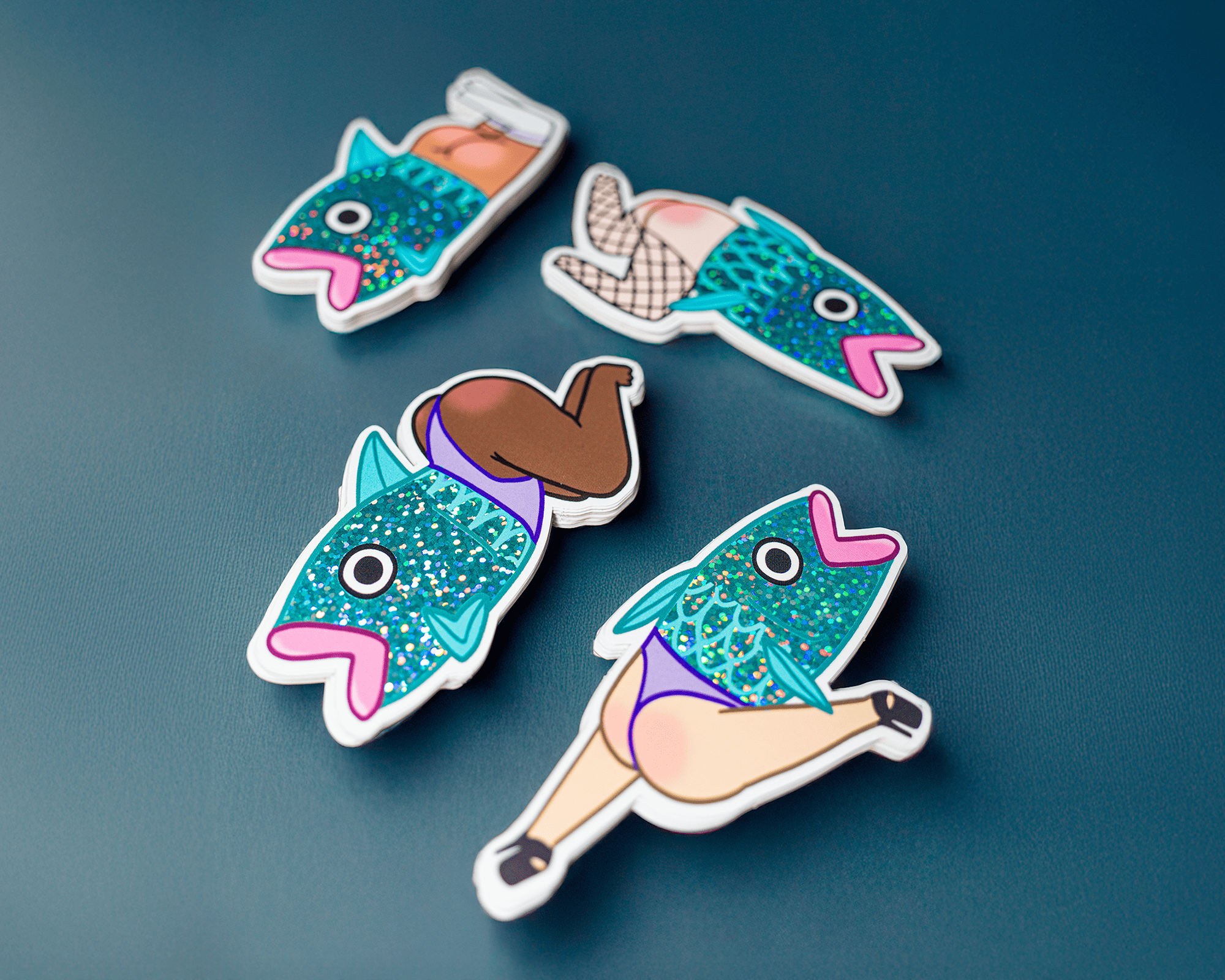 Four colorful glitter stickers of fish with human legs in various poses on a blue surface.