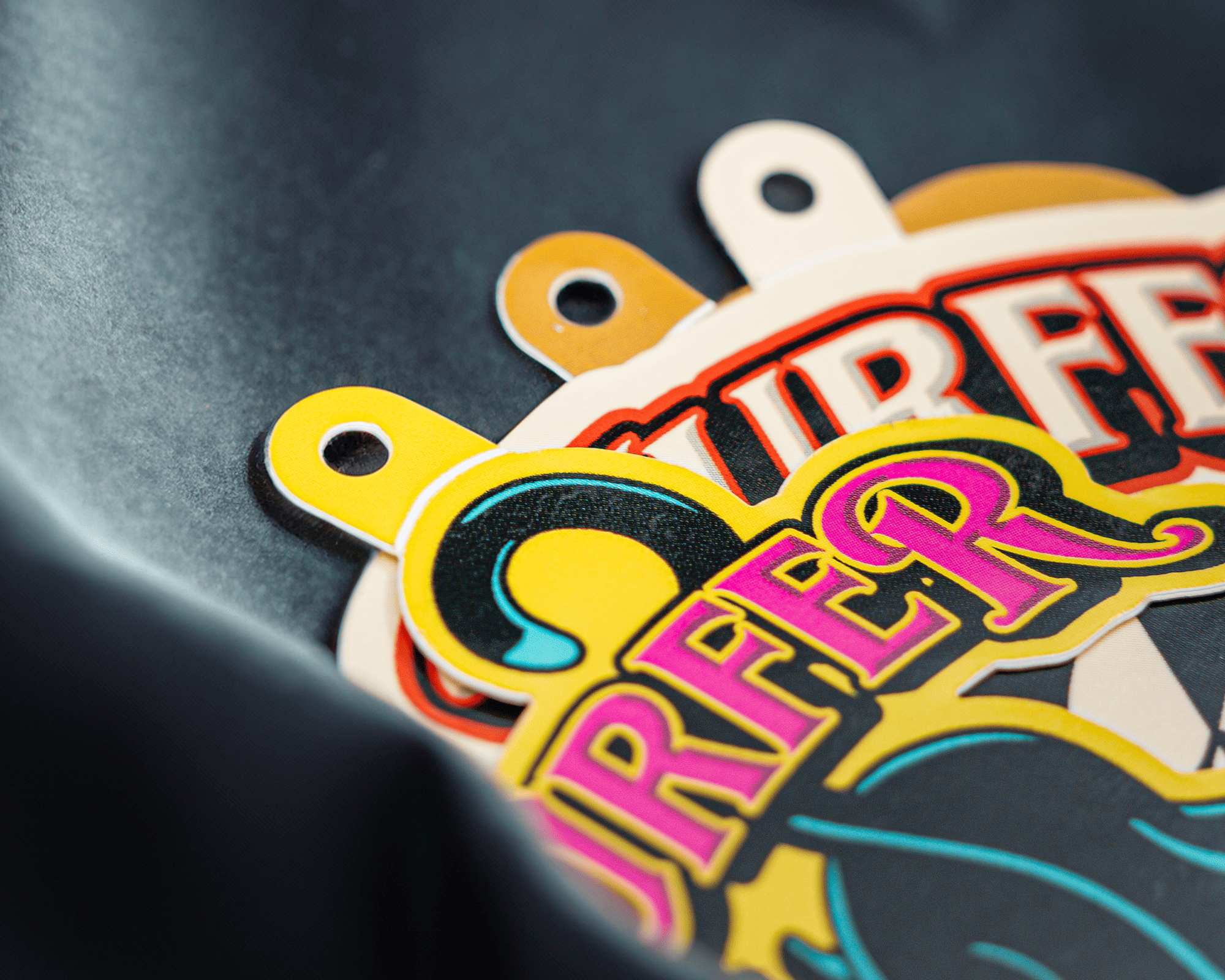 Colorful graphic hang tags with bold letters and circular shapes on a dark background, partially shadowed.