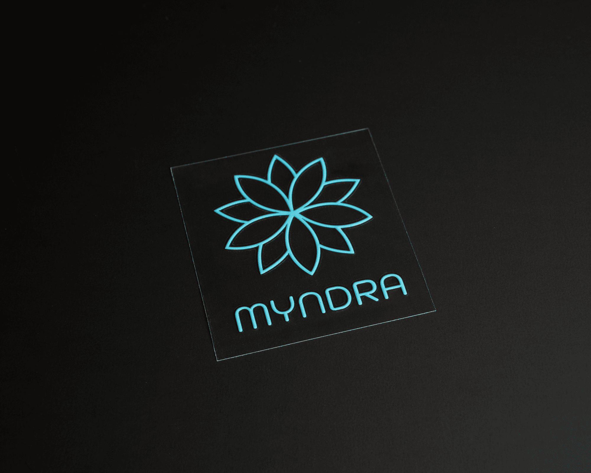 A turquoise geometric flower logo UV DTF transfer sticker with the word "MYNDRA".
