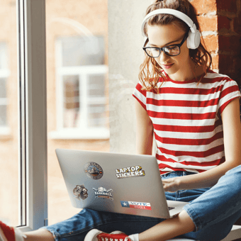 A girl sitting on a window sill using a laptop with custom stickers.