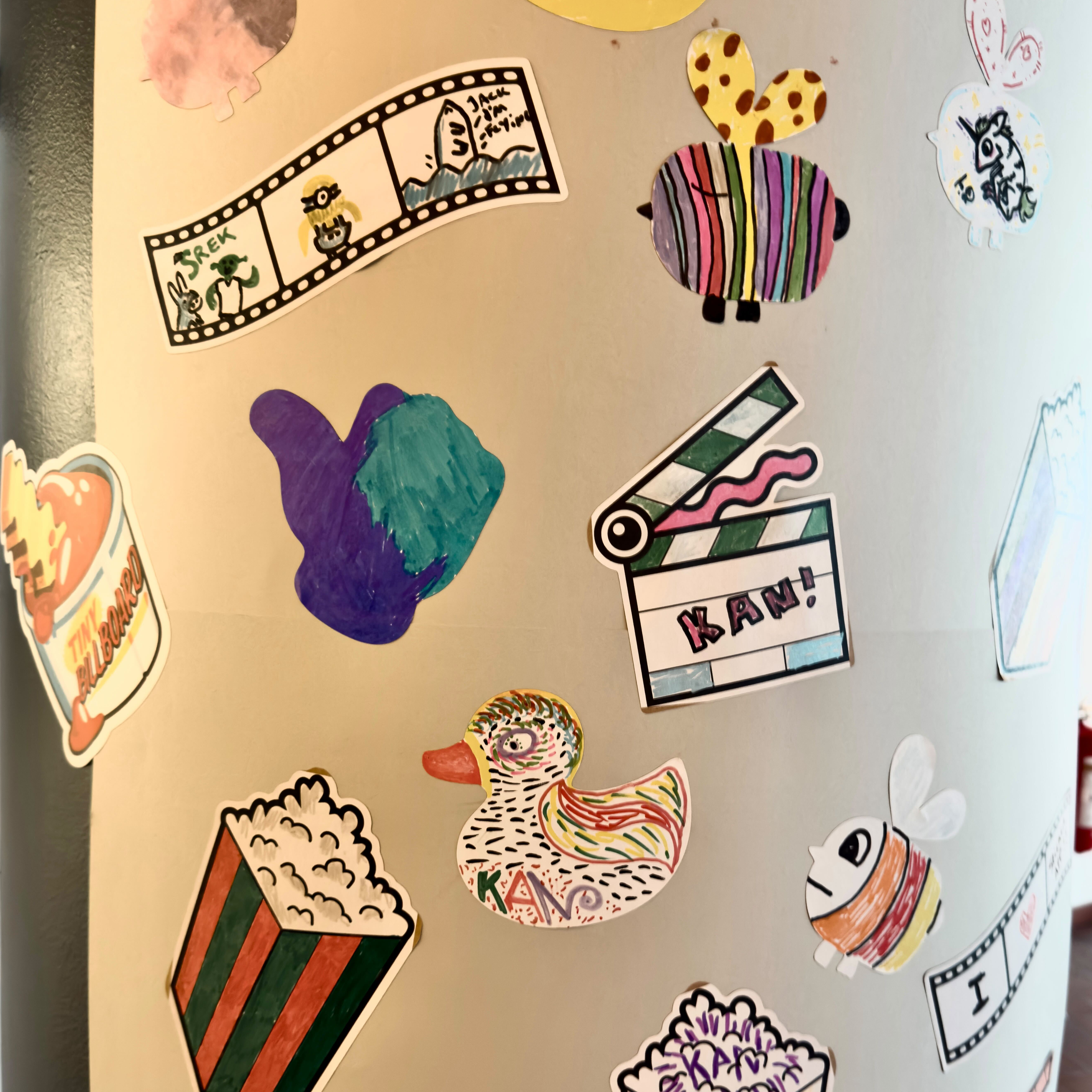 Pillar covered in hand-drawn stickers made by visitors at KAN filmfestival, including popcorn, film strips, a duck and a clapperboard reading "KAN!"