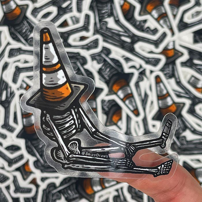 Transparent die-cut sticker of a skeleton sitting on the ground, with a traffic cone on its head, against a background of stickers.